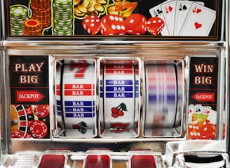 A close-up view of a slot machine with vibrant colors and various gambling symbols such as dice, coins, and playing cards. The reels display a combination of symbols, including bars, cherries, and the number seven. The chrome exterior and colorful details convey the theme of casino and gambling.