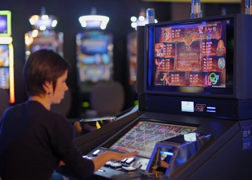 A person is seated at a slot machine console in a casino, focusing intently on the game displayed on the screen. The background shows several other illuminated gaming machines, adding a vibrant and colorful atmosphere to the scene.