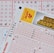 Three lottery tickets are displayed, including Eurojackpot and Super 6. Various numbers are marked on the tickets, with some crossed out and others checked. The Eurojackpot ticket is partially visible with the logo prominently displayed, and a ticket number is visible on one of the tickets.