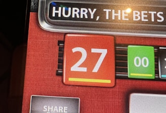 A digital display screen showing a casino betting interface, with text prompting to hurry bets and a highlighted number 27 in red. There are options for betting amounts and a 'share bets' button.