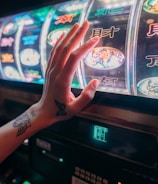 A hand with tattoos reaches towards a brightly lit slot machine, featuring various colorful symbols including a tiger. The image captures the moment of anticipation as the person engages with the machine during a game of chance.